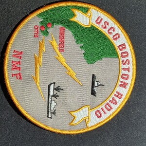 May include: A gray and green embroidered patch with the text "USCG Boston Radio" and a map of the Boston Harbor area with the text "Marshfield" and "Otis".