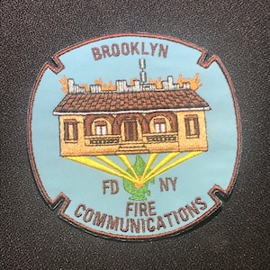 May include: A blue and brown embroidered patch with the text "BROOKLYN FD NY FIRE COMMUNICATIONS" and a depiction of a building with flames on the roof.