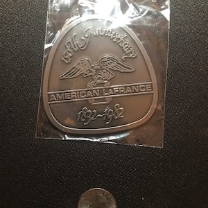 May include: A silver metal commemorative plaque with the text "150th Anniversary", an eagle with outstretched wings, and the text "American LaFrance 1832-1982".