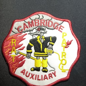 Op de afbeelding: Een witte en rode geborduurde patch met een cartoonrat in een brandweeruniform. De patch zegt "Cambridge Rat Patrol Auxiliary" in een cirkelvormig ontwerp.