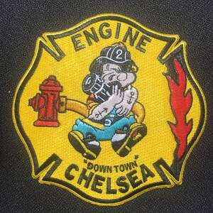 May include: Yellow and black embroidered patch featuring a cartoon firefighter holding a hose and a fire hydrant. The patch reads "Engine" and "Downtown Chelsea" in black.