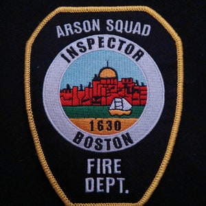 May include: A black and gold embroidered patch with the text "Arson Squad Inspector Boston Fire Dept." and a white circle with a red and green building and the text "1630" inside.
