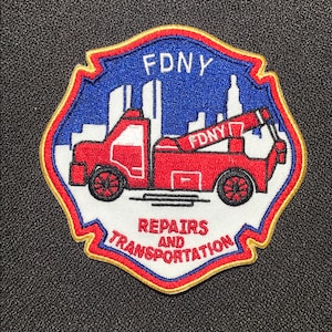Könnte beinhalten: Gestickter Aufnäher mit einem roten Abschleppwagen, dem Text "FDNY" und einer Stadtsilhouette auf blauem Hintergrund. Der Aufnäher enthält auch die Worte "REPAIRS AND TRANSPORTATION" in einem gebogenen Banner.