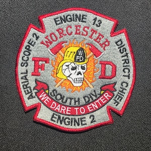 May include: A gray and red embroidered patch with a skull and cross axes. The patch reads "Worcester District Chief, Engine 13, Aerial Scope 2, South Div, We Dare To Enter, Engine 2".