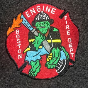 May include: Red and white embroidered patch featuring a green cartoon firefighter holding a hose. The patch reads "Engine" and "Boston Fire Dept."