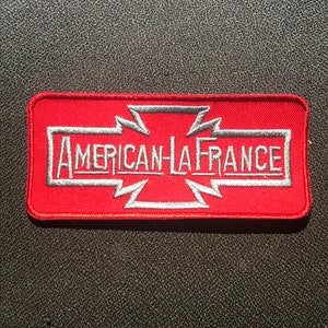 Könnte beinhalten: Roter gestickter Aufnäher mit einem weißen Kreuz und dem Text "American LaFrance" in weiß.