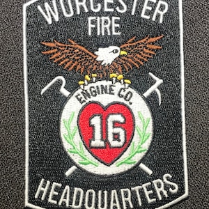 May include: Black and white embroidered patch with the text "Worcester Fire Engine Co. 16 Headquarters" and a white eagle with brown wings on a black background.