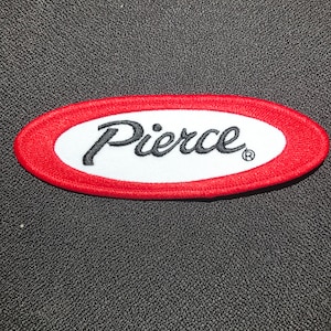 Könnte beinhalten: Roter ovaler Patch mit einem weißen Oval im Inneren. Das Wort "Pierce" ist in Schwarz auf das weiße Oval gestickt.
