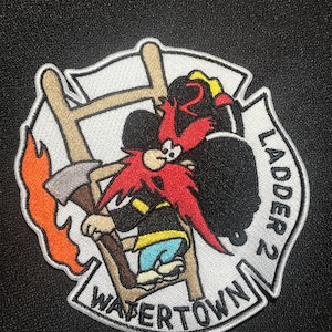 May include: A white and red embroidered patch featuring a cartoon character climbing a ladder. The character is holding an axe and has a red beard. The patch reads "Watertown Ladder 2" around the edge.