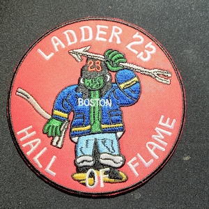 May include: A red, white, and blue embroidered patch with a cartoon firefighter holding a ladder and the text "Ladder 23 Hall of Fame Boston".