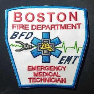 Può includere: Toppa bianca con bordo blu, con il testo "BOSTON FIRE DEPARTMENT BFD EMT EMERGENCY MEDICAL TECHNICIAN" in lettere rosse e nere. Una stella della vita blu con un casco giallo è al centro.