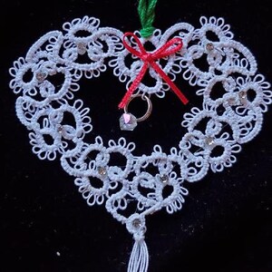 May include: White lace heart ornament with a red ribbon and a crystal pendant. The ornament has a tassel hanging from the bottom.