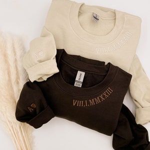 May include: A set of three ceramic mugs with a speckled, cream-colored glaze. Each mug features a different hand-painted floral design in shades of blue, green, and yellow. The mugs have a simple, rounded shape and a comfortable handle.