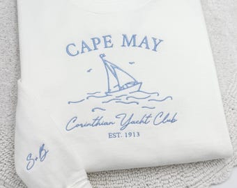 May include: White long-sleeved sweatshirt with blue embroidered text and sailboat graphic. The text reads "CAPE MAY", "Corinthian Yacht Club", and "EST. 1913". The sleeve has the embroidered initials "S & G".