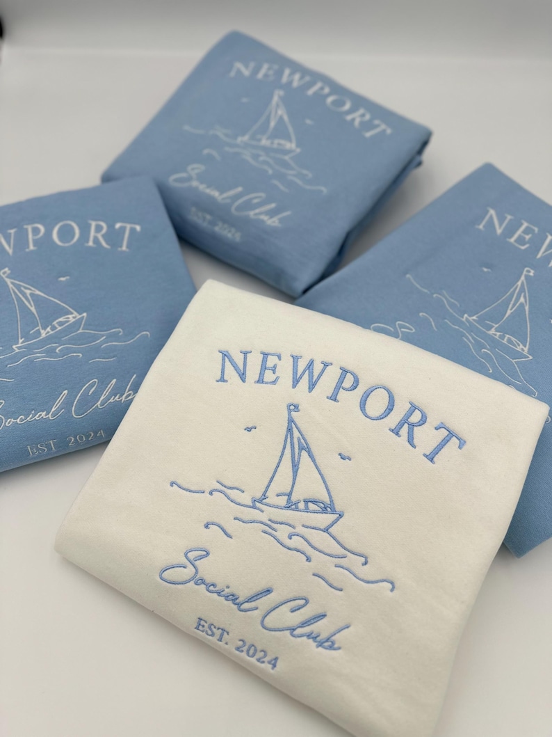 May include: Three folded white and light blue t-shirts with the text "NEWPORT Social Club EST. 2024" and a sailboat graphic.