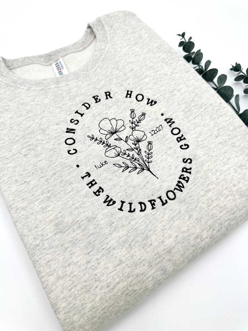 May include: Gray sweatshirt with a black graphic design that says "Consider how many grow the wildflowers. Luke 12:27"