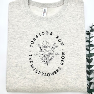 May include: Gray sweatshirt with a black circle design featuring a floral illustration and the text "Consider how the wildflowers grow. Luke 12:27"