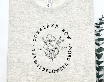 May include: Gray sweatshirt with a black circle design featuring a floral illustration and the text "Consider how the wildflowers grow. Luke 12:27"