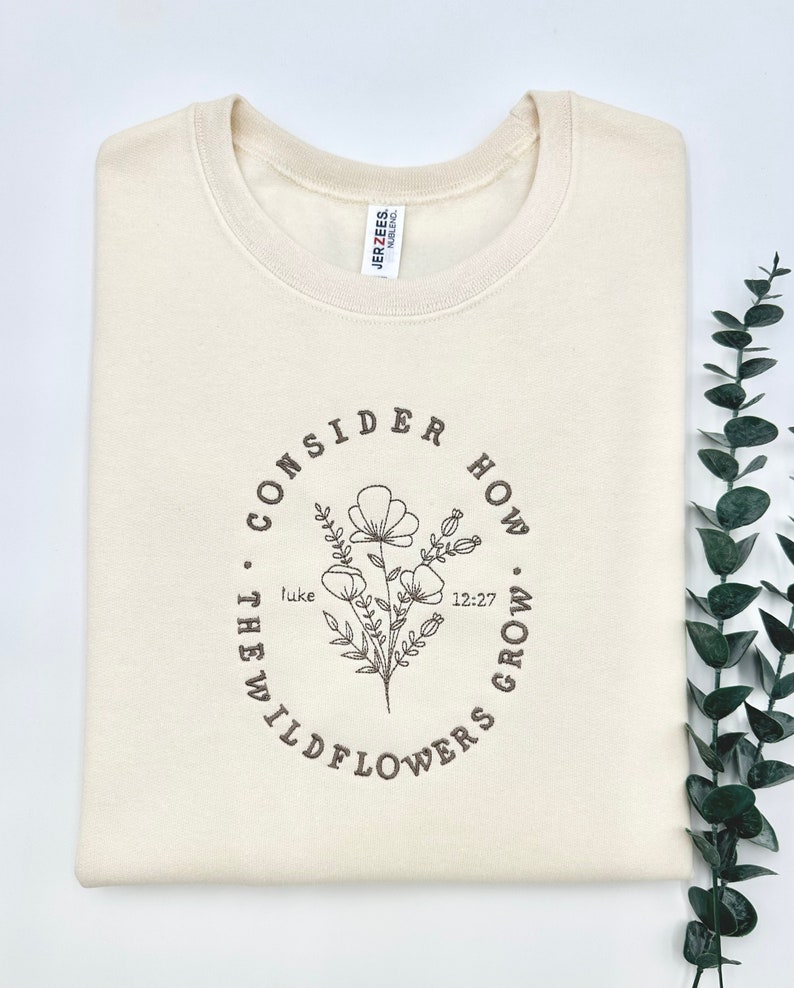 May include: A cream-colored sweatshirt with a brown graphic design that says "Consider how the wildflowers grow" with a floral illustration and the text "Luke 12:27".