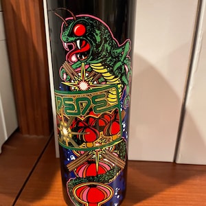 May include: A black stainless steel tumbler with a colorful graphic design featuring a green insect with red eyes, a yellow and green snake, and red and pink mushrooms. The text "REBEL" is visible in the design.