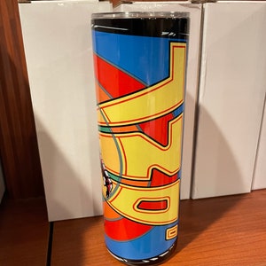 May include: A stainless steel tumbler with a colorful geometric design featuring a yellow, red, and blue pattern. The tumbler has a black lid and a black base.