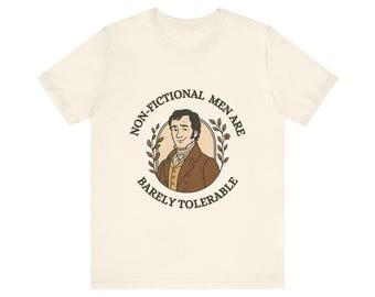 May include: Cream-colored t-shirt featuring a cartoon illustration of a man in a brown coat and the text "NON-FICTIONAL MEN ARE BARELY TOLERABLE" in a circular design. The design includes a laurel wreath around the man's portrait.