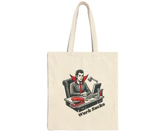 May include: Beige tote bag featuring a cartoon illustration of a vampire at a desk. The vampire is wearing a suit and tie, and the desk has a computer, stapler, and lamp. The text "Work Sucks" is printed below the desk.