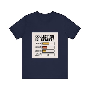 May include: Navy blue t-shirt with a graphic that reads "COLLECTING IRL DEBUFFS" above a series of bars indicating levels of tiredness, hunger, anxiety, and social battery. The social battery is empty.