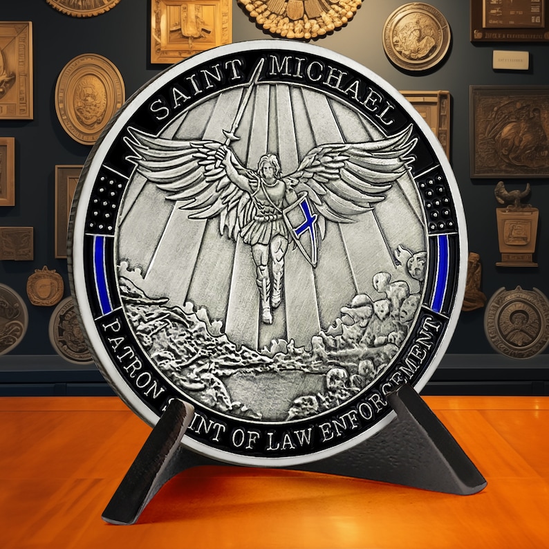 May include: A silver-toned round coin with a blue and black border. The coin features a depiction of Saint Michael, a winged angel, holding a sword and shield. The text "SAINT MICHAEL PATRON SAINT OF LAW ENFORCEMENT" is inscribed around the edge of the coin.