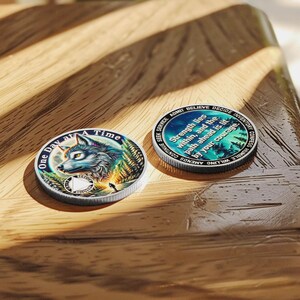 May include: Two silver-toned round coins with a wolf design and inspirational text. The front of the coin features a wolf's head with a blue and green forest background. The back of the coin features a blue and green aurora borealis design with the text "Strength lies within, and the path ahead is lit by your courage".