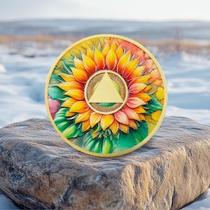 Könnte beinhalten: Ein kreisförmiges Medaillon mit einem leuchtend bunten Sonnenblumenmotiv mit gelben, orangefarbenen und grünen Blütenblättern. In der Mitte der Sonnenblume befindet sich ein glattes, goldfarbenes Dreieck in einem strukturierten, goldenen Rand.