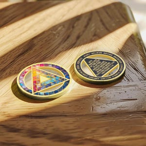 Puede incluir: Dos medallones circulares dorados. Uno presenta un dise&ntilde;o geom&eacute;trico colorido con un tri&aacute;ngulo en el centro. El otro tiene texto alrededor del borde y en el centro, incluyendo "BUT THE PATH OF THE JUST IS AS THE SHINING LIGHT".