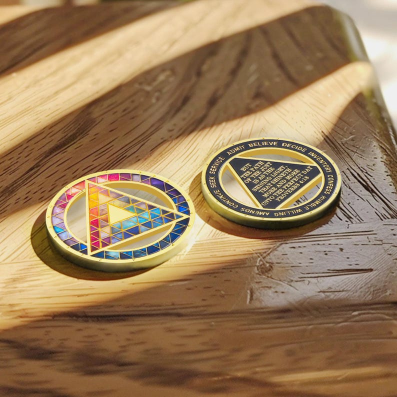 Puede incluir: Dos medallones circulares dorados. Uno presenta un dise&ntilde;o geom&eacute;trico colorido con un tri&aacute;ngulo en el centro. El otro tiene texto alrededor del borde y en el centro, incluyendo "BUT THE PATH OF THE JUST IS AS THE SHINING LIGHT".