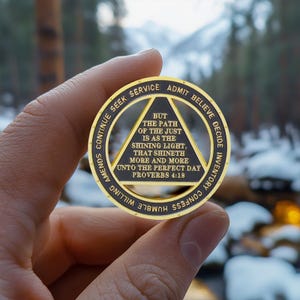 Puede incluir: Una moneda dorada con texto negro y un dise&ntilde;o triangular. La moneda presenta las palabras "ADMITIR, CREER, DECIDIR, INVENTARIO, CONFESAR, DISPUESTO, HUMILDE, ENMENDAR, CONTINUAR, BUSCAR, SERVICIO". El texto central dice "PERO EL CAMINO DEL JUSTO ES COMO LA LUZ RESPLANDECIENTE, QUE RESPLANDECE M&Aacute;S Y M&Aacute;S HASTA EL D&Iacute;A PERFECTO PROVERBIOS 4:18."