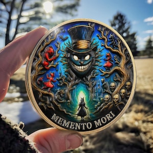 Op de afbeelding: Een ronde, gedetailleerde munt met een grijnzende Cheshire Cat in een hoge hoed, omringd door grillige figuren en de tekst "Memento Mori". De munt heeft een gouden rand en een blauwgroene achtergrond.