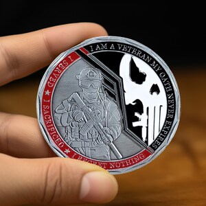 May include: A silver challenge coin with a red and black design. The coin features a soldier holding a rifle, a skull, and the text "I am a veteran, my oath never expires. I sacrificed, I served, I regret nothing."