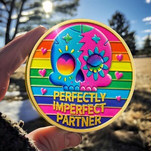 May include: A gold-colored round pin with a rainbow-colored background and a colorful skull design. The text "PERFECTLY IMPERFECT PARTNER" is written in pink and white letters.