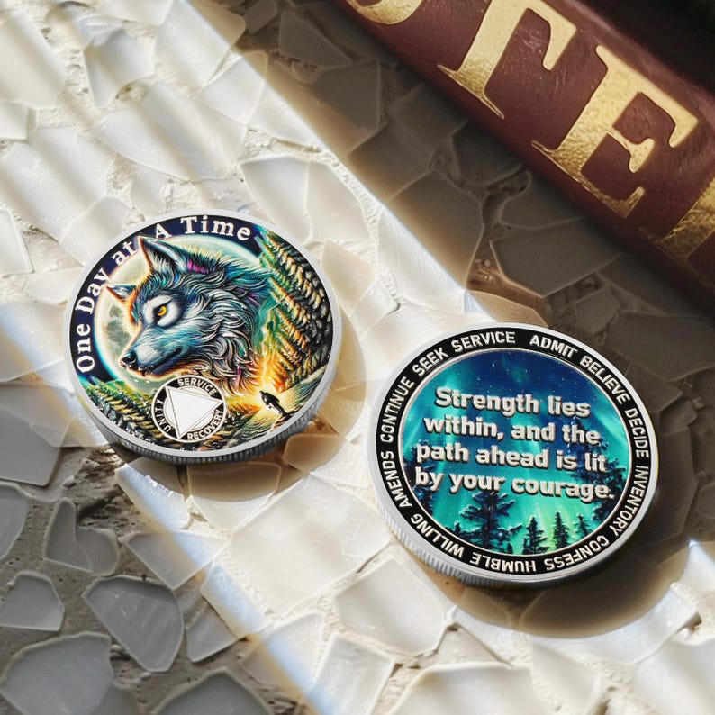 May include: Two silver coins with colorful designs. One coin features a wolf with a blue, green, and orange design and the text "One Day at A Time". The other coin features a blue, green, and purple design with the text "Strength lies within, and the path ahead is lit by your courage."
