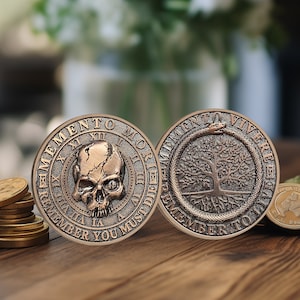 Op de afbeelding: Twee ronde, koperkleurige munten met verhoogde randen. De eerste munt heeft een schedel met een gebarsten gezicht en de woorden "Memento Mori" en "Denk eraan dat je moet sterven". De tweede munt heeft een boom met wortels en een slang die om de stam is gewikkeld met de woorden "Memento Vivere" en "Denk eraan om te leven".