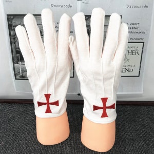 Könnte beinhalten: Ein Paar weiße Baumwollhandschuhe mit roten gestickten Kreuzen auf der Rückseite jeder Hand.