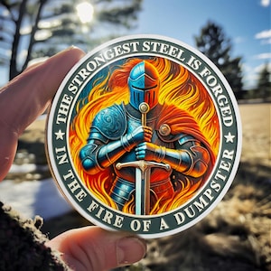 May include: A circular sticker featuring a knight in blue and red armor holding a sword, surrounded by orange and yellow flames. The border text reads, THE STRONGEST STEEL IS FORGED IN THE FIRE OF A DUMPSTER, with a star on each side of the text.