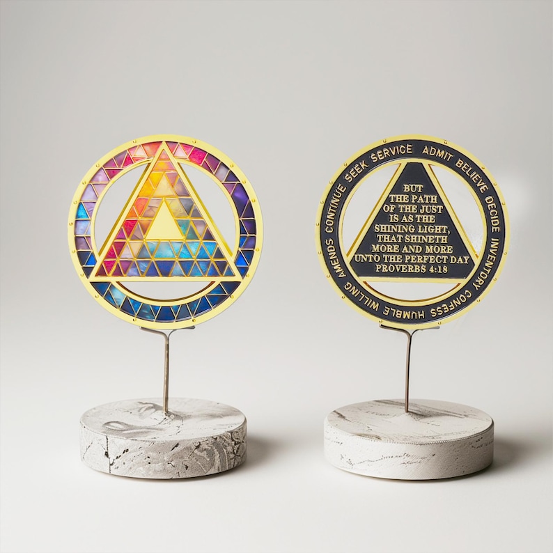 Puede incluir: Dos piezas decorativas de arte en metal dorado. Una presenta un dise&ntilde;o de vidriera de colores dentro de un c&iacute;rculo y un tri&aacute;ngulo. La otra tiene el texto "BUT THE PATH OF THE JUST IS AS THE SHINING LIGHT, THAT SHINETH MORE AND MORE UNTO THE PERFECT DAY PROVERBS 4:18."