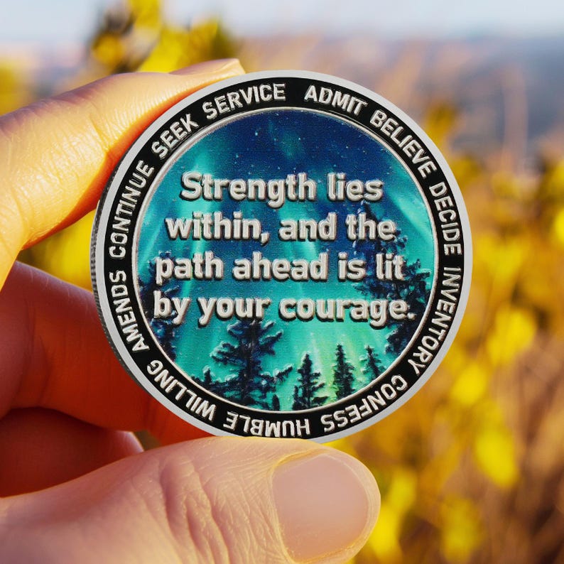 May include: A silver coin with a blue and green aurora borealis design. The coin has the words "Strength lies within, and the path ahead is lit by your courage." around the edge.