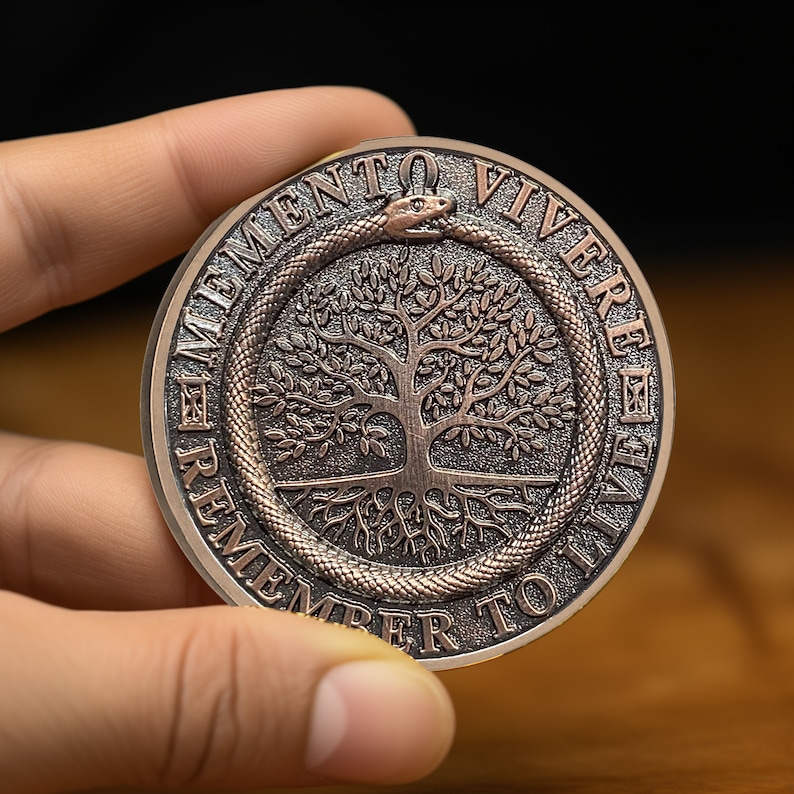 Op de afbeelding: Een koperkleurige munt met een levensboomontwerp en de woorden "Memento Vivere Remember To Live" rond de rand.