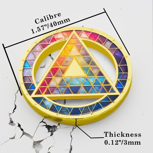 Puede incluir: Un colgante circular dorado con un dise&ntilde;o geom&eacute;trico colorido. El colgante presenta un tri&aacute;ngulo dentro de un c&iacute;rculo, lleno de tri&aacute;ngulos de varios colores. El texto "Calibre 1.57"/40mm" y "Thickness 0.12"/3mm" son visibles.