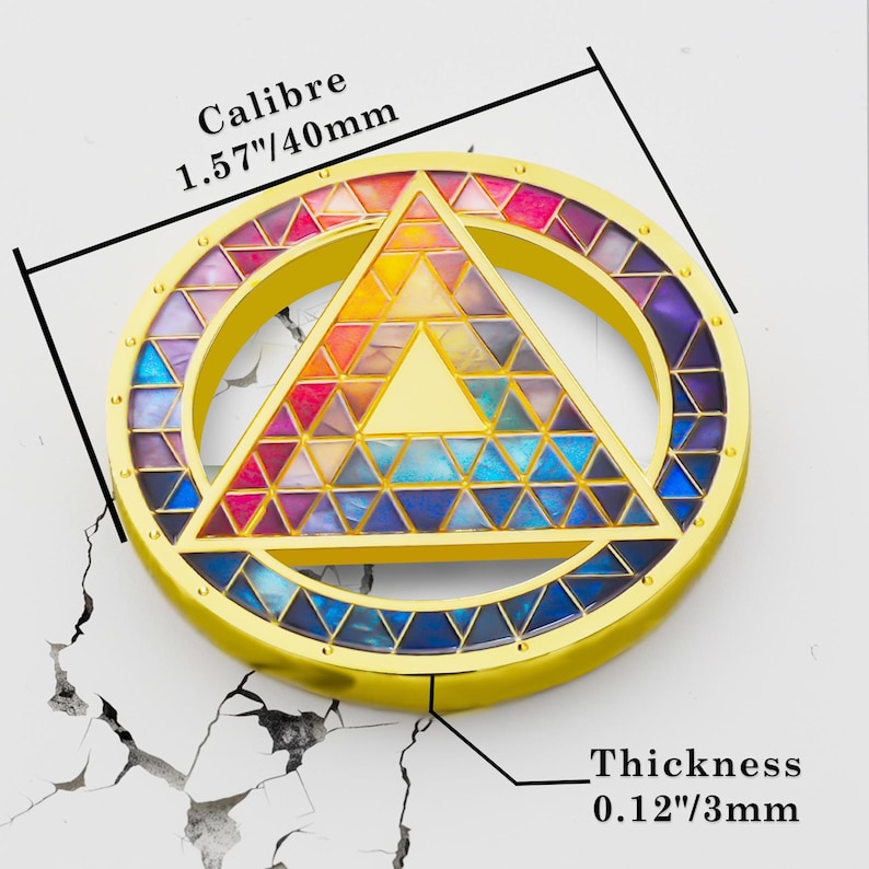 Puede incluir: Un colgante circular dorado con un dise&ntilde;o geom&eacute;trico colorido. El colgante presenta un tri&aacute;ngulo dentro de un c&iacute;rculo, lleno de tri&aacute;ngulos de varios colores. El texto "Calibre 1.57"/40mm" y "Thickness 0.12"/3mm" son visibles.