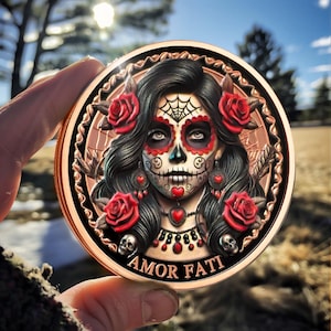 May include: A round copper coin with a detailed image of a woman with a sugar skull makeup, red roses, and the words "AMOR FATI" on the bottom.