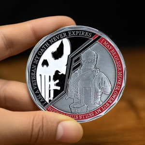 May include: A silver and red round challenge coin with a skull and crossbones on one side and a soldier on the other. The text on the coin reads "I am a Veteran my Oath Never Expires I may be older move slower but my skills still remain".