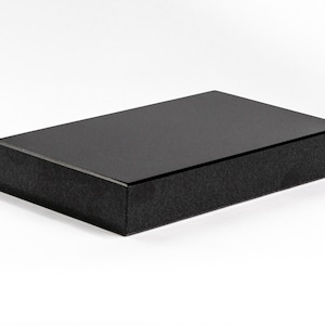 May include: A black rectangular box with a smooth, glossy top and a textured bottom. The box is made of a sturdy material and has a sleek, modern design.