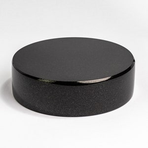 May include: A black round pedestal made of polished granite. The pedestal is smooth and has a slightly textured surface.